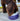 An Irish Water Spaniel eating from a purple ceramic bowl with a white rim. The bowl is on decking outside. The dog has a curly brown coat.