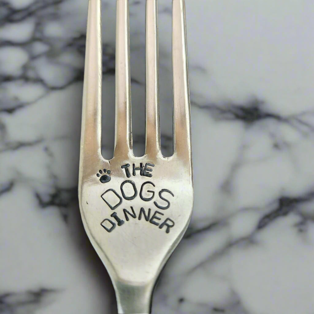 Silver fork with 'The Dog's Dinner' engraving on a marble surface